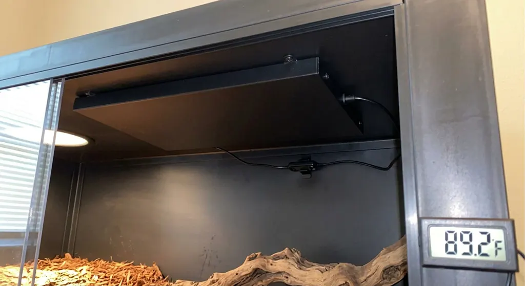Close-up phone photo of a Radiant Heat Panel and digital proportional thermostat sensor mounted inside a snake enclosure.